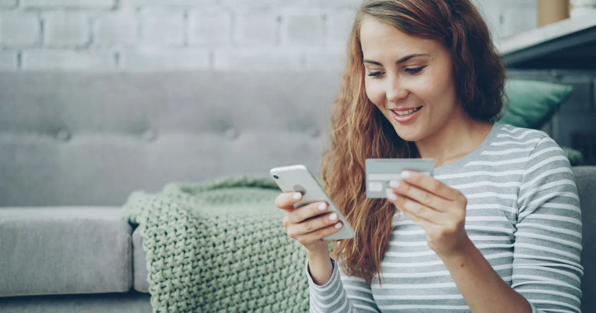 Woman holding a smartphone and bank card, about to pay for an online order